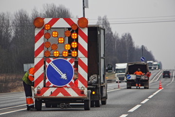 Road works, a big bright mobile sign with red white stripes, direction of the detour and a yellow...