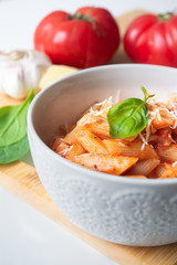 Classic italian penne pasta arabiata with its ingredients in the background: fresh tomatoes, basil, garlic and parmesan cheese