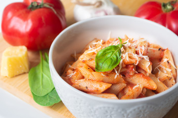 Classic italian penne pasta arabiata with its ingredients in the background: fresh tomatoes, basil, garlic and parmesan cheese