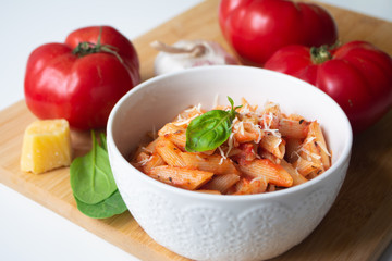 Classic italian penne pasta arabiata with its ingredients in the background: fresh tomatoes, basil, garlic and parmesan cheese