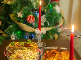 Fragment of a table with a Christmas dinner with burning candles on a background of the Christmas tree