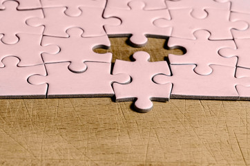 the unexpected solution. pink jigsaw/puzzle with one piece at wrong position, on a wooden table...