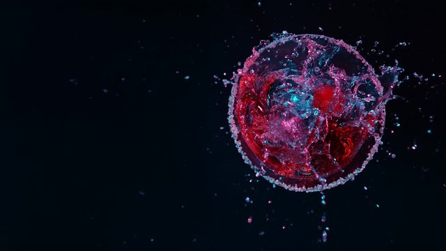 Super Slow motion shot of ice cubes into martini. Red cherry is falling into a glass of Dry Martini cocktail. Top view.
