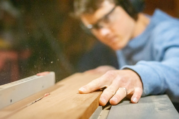 Fototapeta na wymiar Sawdust flies as man uses table saw on hardwood in wood shop