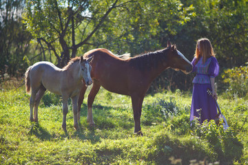 a girl with a guitar stands next to a horse and a foal