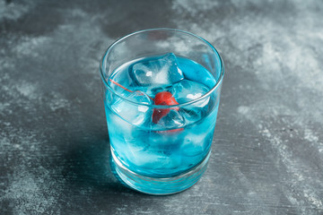 Blue old fashioned cocktail with cherry on the rustic background. Selective focus. Shallow depth of field.
