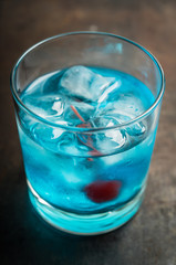 Blue old fashioned cocktail with cherry on the rustic background. Selective focus. Shallow depth of field.
