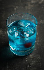Blue old fashioned cocktail with cherry on the rustic background. Selective focus. Shallow depth of field.
