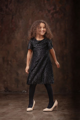 Fototapeta premium Little girl in oversized shoes near black wall with space for text.