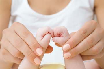 Young mother hands holding her infant little hands. Baby fists. Playing with baby. Lovely, emotional moment. Relationship concept. Closeup.