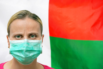 Masked woman face looking at the camera on flag Madagascar background. The concept of attention to the worldwide spread of the coronavirus worldwide. Coronavirus, virus in Madagascar.