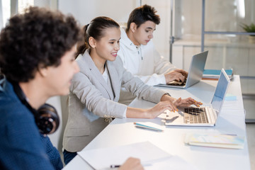 Row of teenage classmates sitting by desk at lesson and discussing online data