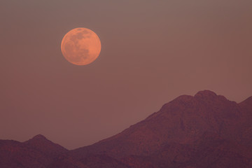  waiting for and then seeing a full moon rise from behind a colorful desert mountain with its thin...