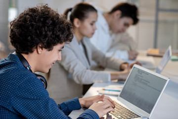 Successful teenage student looking at laptop display while entering information