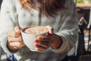 female hand holding cup of hot cocoa or chocolate on wooden table, close up