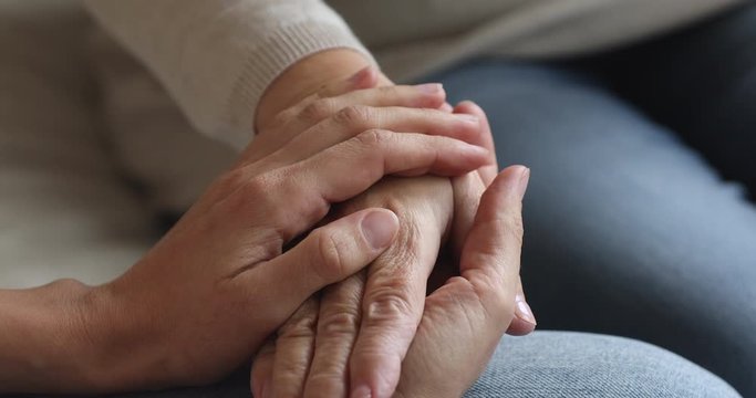 Close up compassionate young woman stroking hand on middle aged mature mom, having trustful conversation indoors. Kind grown up devoted daughter supporting senior old mother, showing love care.