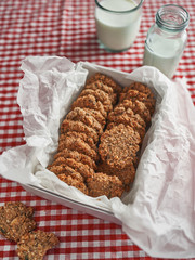 Cookie tin filled with oat cookies beside cold milk