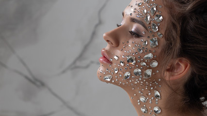Fantastic fashion portrait of a young beautiful woman with transparent crystals on her face and...