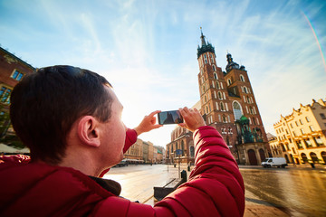 Young man tourist making photo of the famous St. Mary's Basilica on the Market square during the sunrise in Krakow, Poland