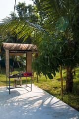 Wicker gazebo among tropical palms with yoga mats. A place for outdoor yoga in India, Kerala.