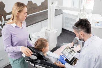 Young contemporary dentist showing dental x-ray in tablet to his little patient