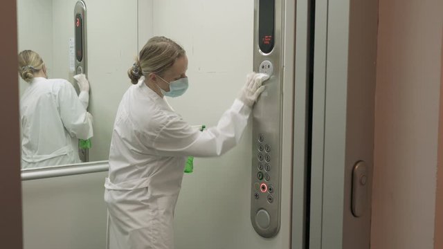 Woman using wet wipe and alcohol sanitizer spray to clean an elevator push button control panel. Disinfection, cleanliness and health care, Anti Coronavirus COVID-19