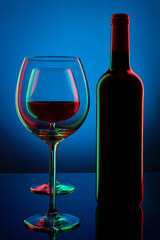 Red wine bottle with two glasses in a colored light on blue background.