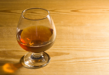 Glass glass with cognac on a wooden table. Free space for text on the side.