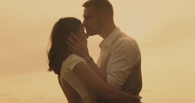 Couple embracing man kissing woman. Tender groom stroking bride's face in sunlight with hands touching face. Real-time, hand-held shot, close up, 4K.