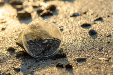 Fototapeta na wymiar Rubbish plastic cup with sand in morning sunrise at beach