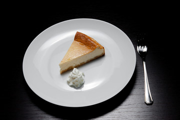 Slice of Cheesecake On White Plate with cream.Slice of tasty cake on white plate served with dessert fork