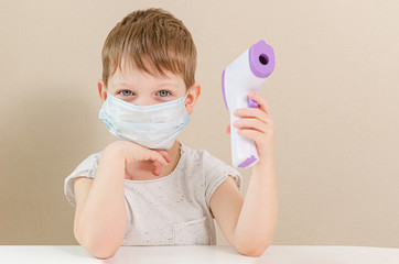 Cute four-year-old boy in a medical mask plays a doctor and measures the temperature with a...