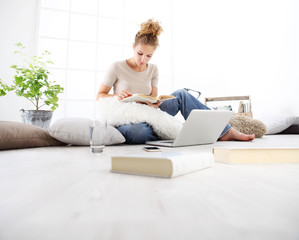 young woman sitting in living room reading a book with your computer nearby, stay at home concept