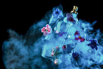A glass perfume bottle shatters and bright spring flowers and clouds of blue and purple vapor burst out of it against a dark background