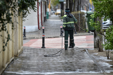 Public janitor deep cleaning the sidewalk with high pressure disinfectant solution in times of...