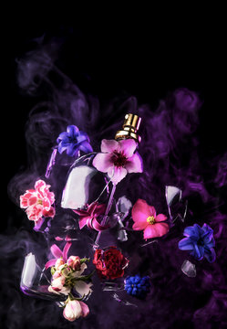 A glass perfume bottle shatters and bright spring flowers and clouds of blue and purple vapor burst out of it against a dark background