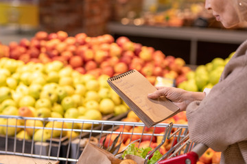 Mature consumer with notepad over food products looking through shopping list