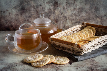 Sesame crackers in a wicker basket on a gray background, a Cup of hot tea and a teapot with tea on a gray background