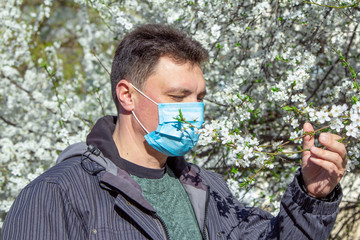 Man, wearing medical mask, protecting from virus and flu, standing near blooming cherry tree,...