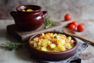 Hot roast of potatoes and pork in a beautiful plate, cooked in clay pots on a gray background