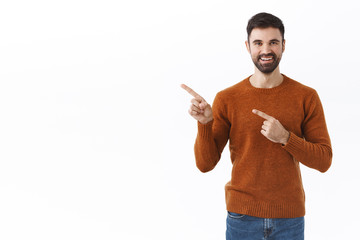 Handsome bearded man in sweatshirt, pointing fingers left at copy space blank for promo banner,...