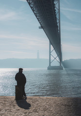 Solo man on a wharf underneath Ponte 25 de Abril in Lisbon, Portugal