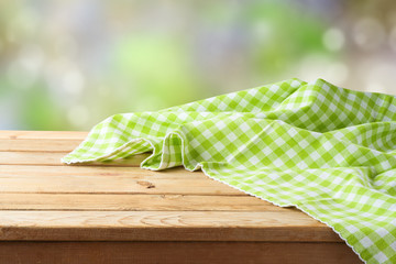 Empty wooden table with green checked tablecloth over green bokeh background.