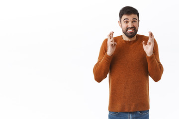 Portrait of nervous handsome bearded guy clench teeth worried, cross fingers good luck, praying and awaiting hopeful for good news, making wish standing white background