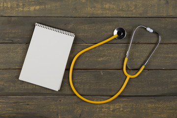 Medical and health care concept - yellow stethoscope and blank spiral notepad on wooden background
