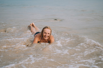 Happy smiling excited elderly senior woman tourist playing in water and swimming in the big waves on the ocean sea beach. Traveling along Asia, active lifestyle concept.