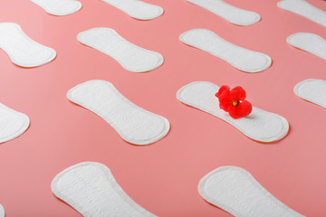 Sanitary pads on a pink background in the form of a diagonal pattern of repetitions, with a red flower on the pad.
