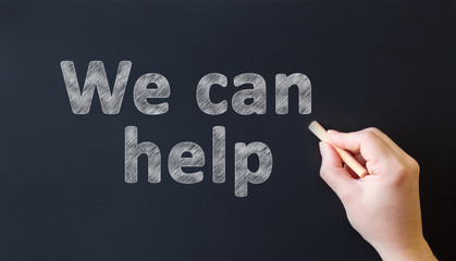 We can help - chalk inscription on a black chalk board. Hand with chalk writes text