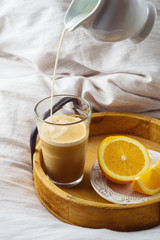 Coffee with milk and fresh oranges on wooden tray on morning bed background