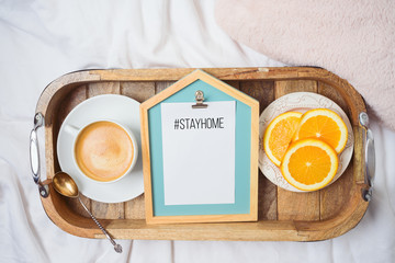 Coffee cup and fresh oranges on wooden tray on morning bed background. Stay at home concept. Top view from above